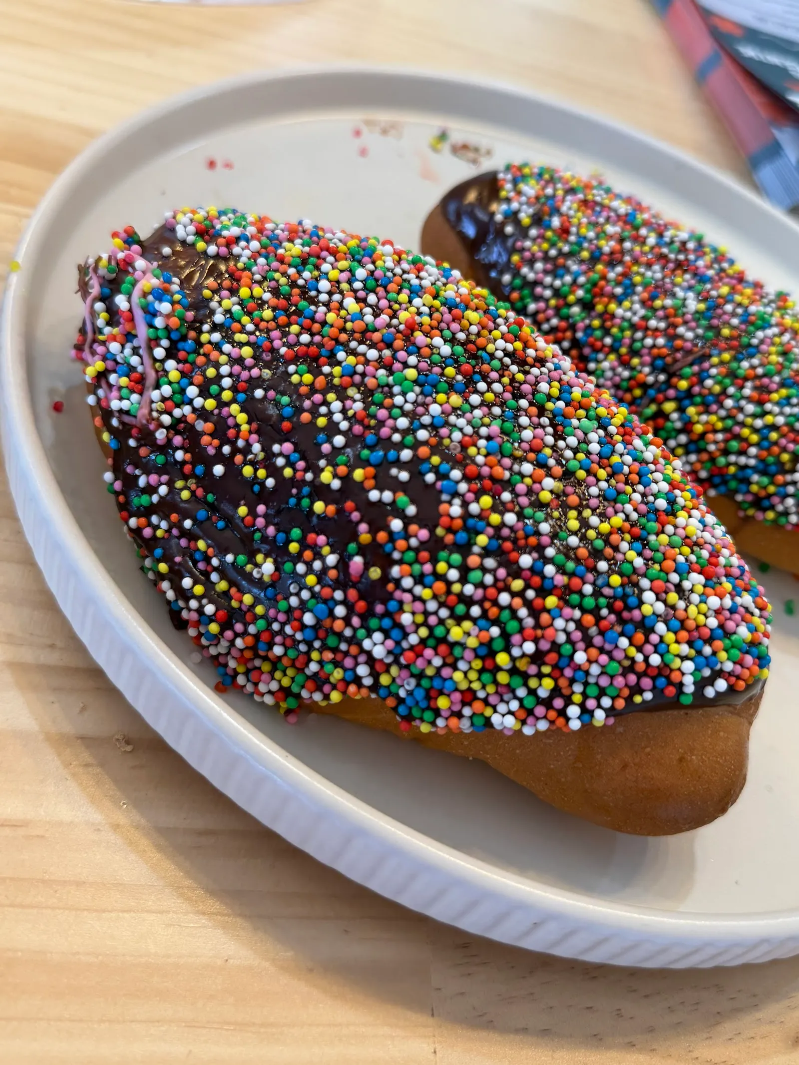 Two chocolate sprinkle finger buns with rainbow hundreds-and-thousands on a white plate