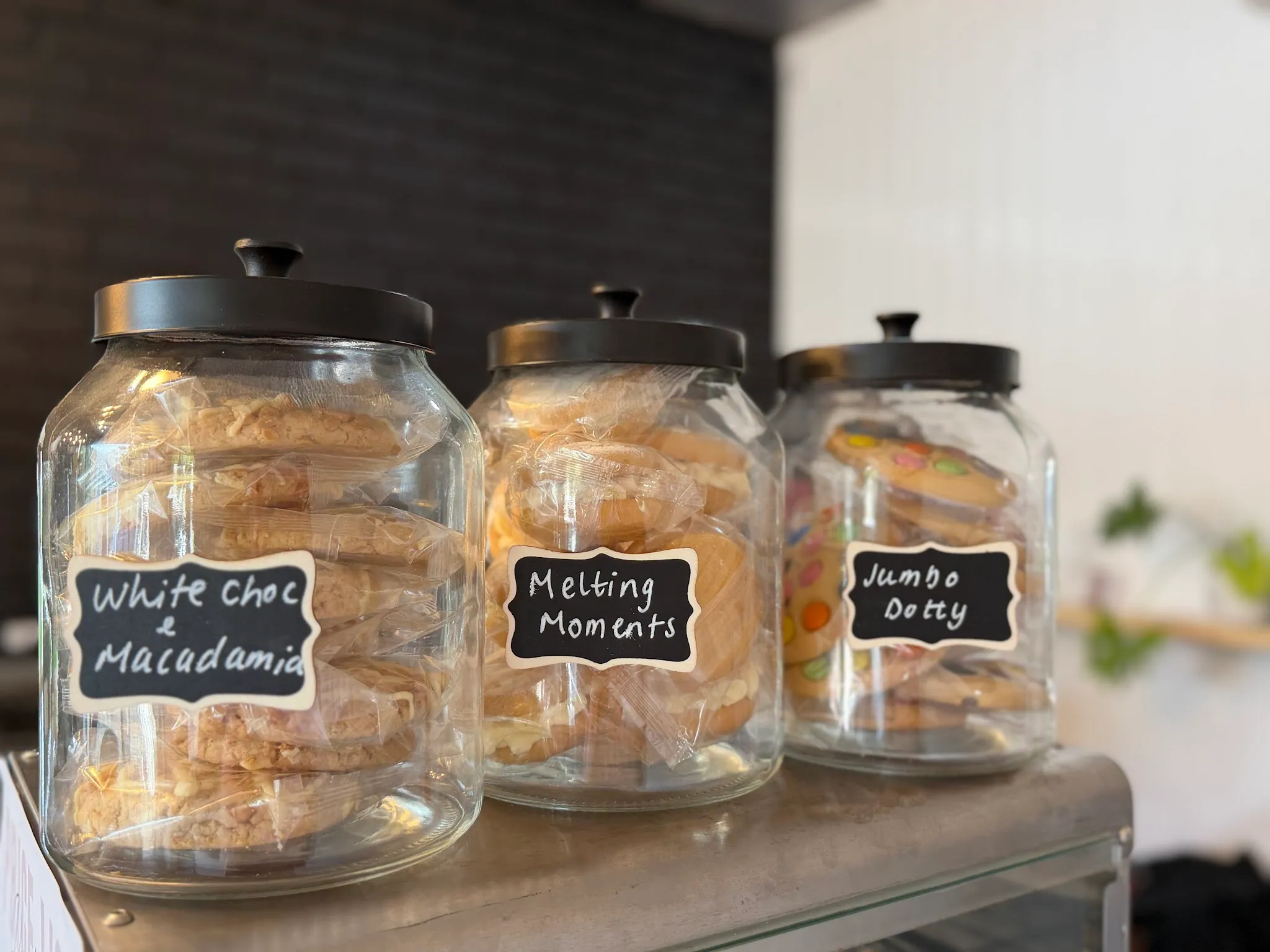 Three glass jars of labelled cookies on a counter cart inside the cafe