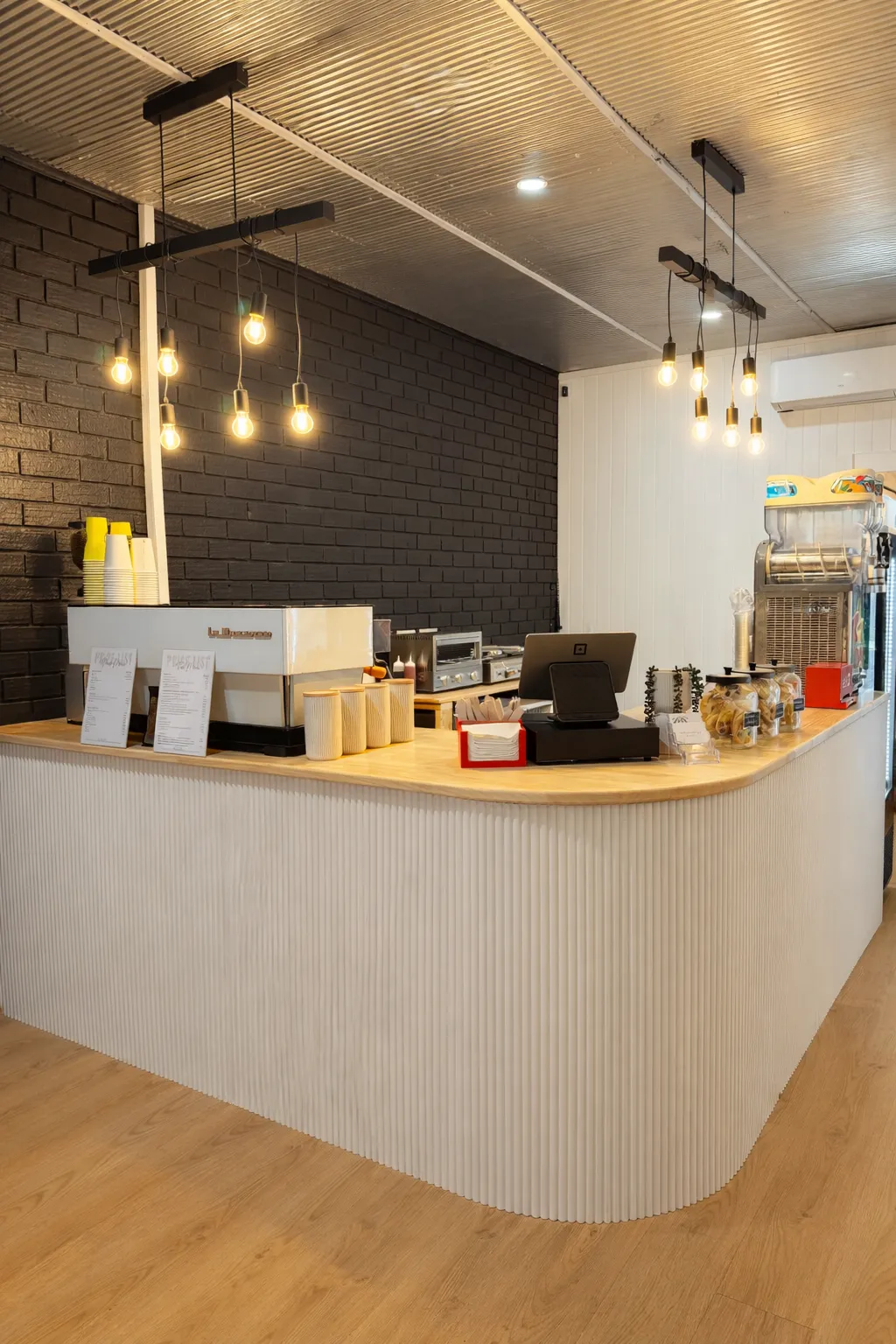 Cafe service counter with fluted base, timber top and Edison pendant lights against black brick