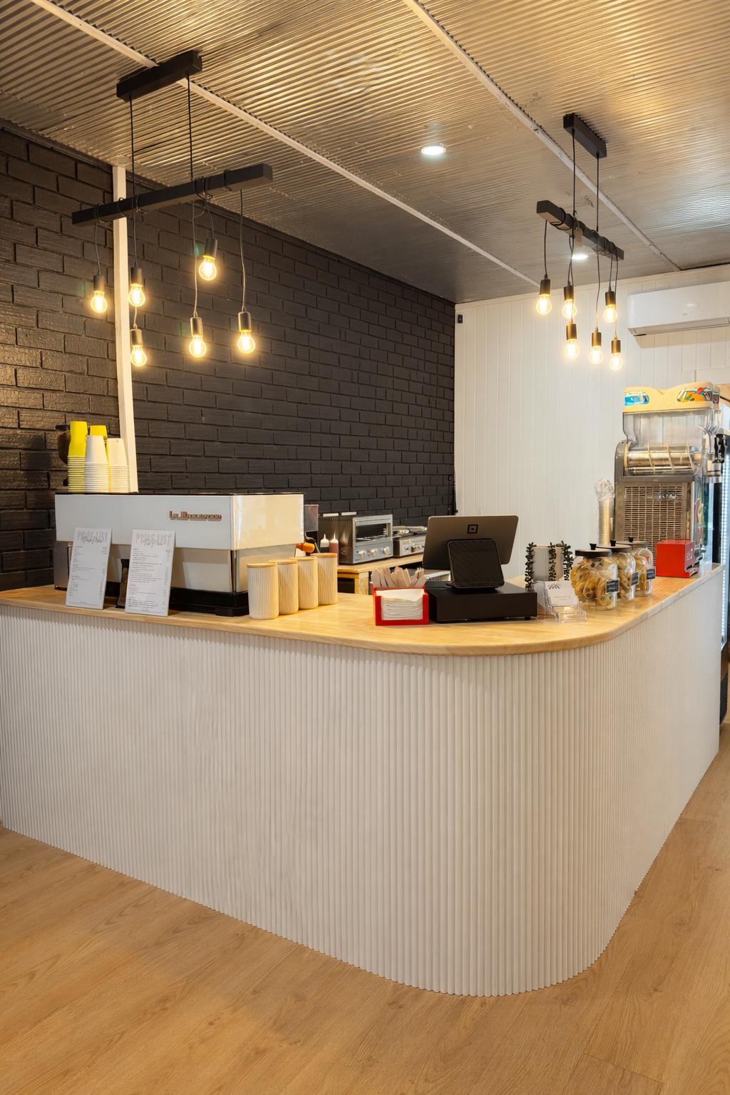 Cafe service counter with fluted base, timber top and Edison pendant lights against black brick