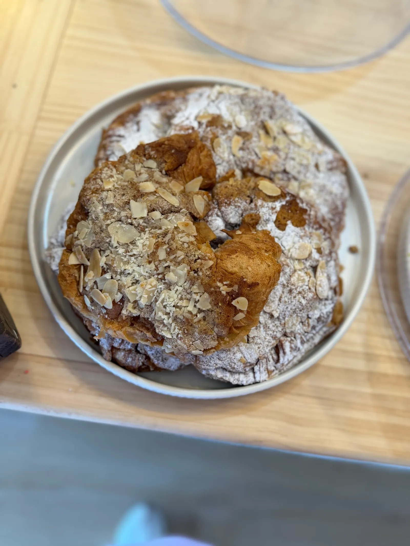 Almond croissant dusted with icing sugar and flaked almonds on a metal plate