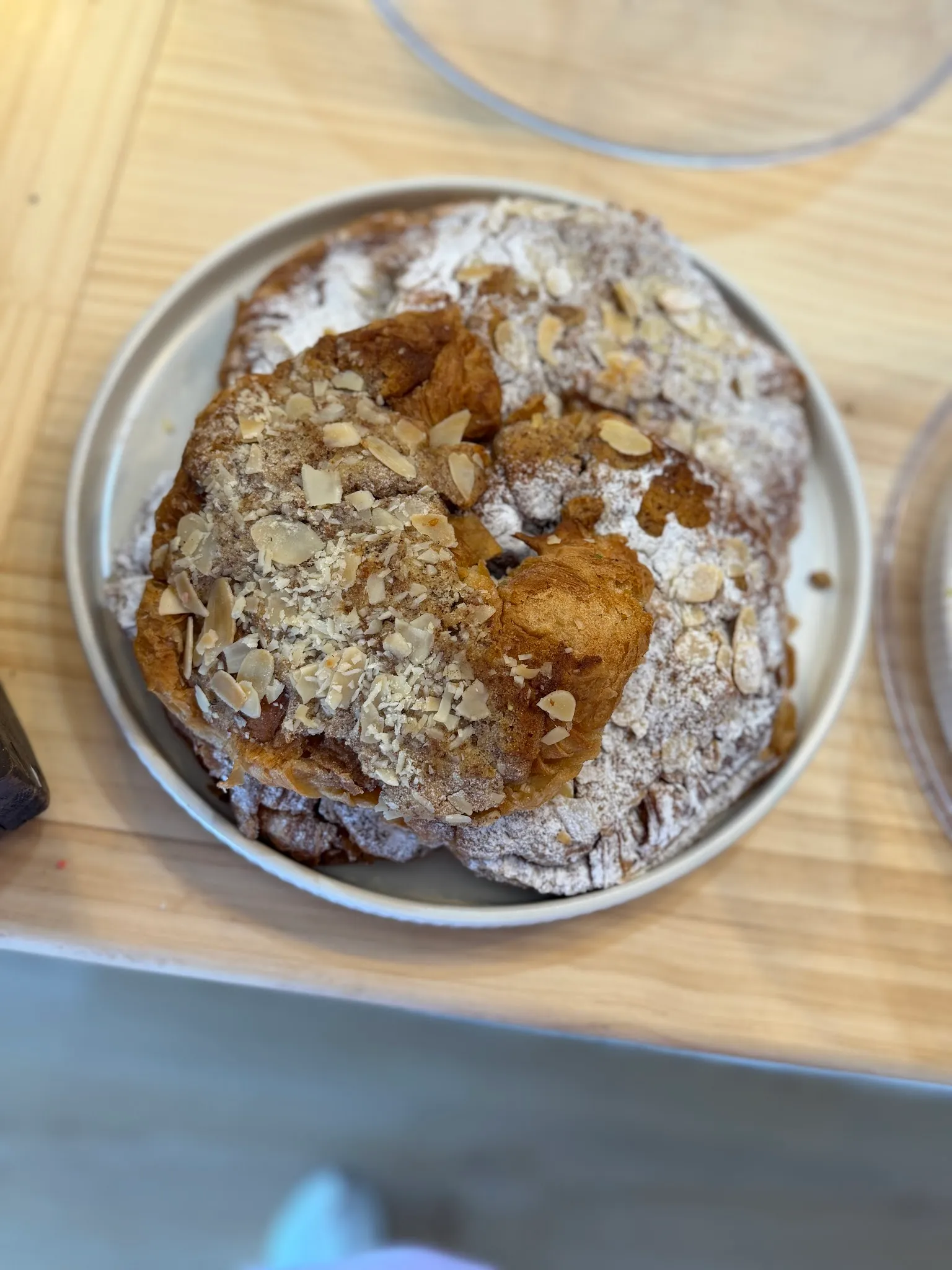 Almond croissant dusted with icing sugar and flaked almonds on a metal plate