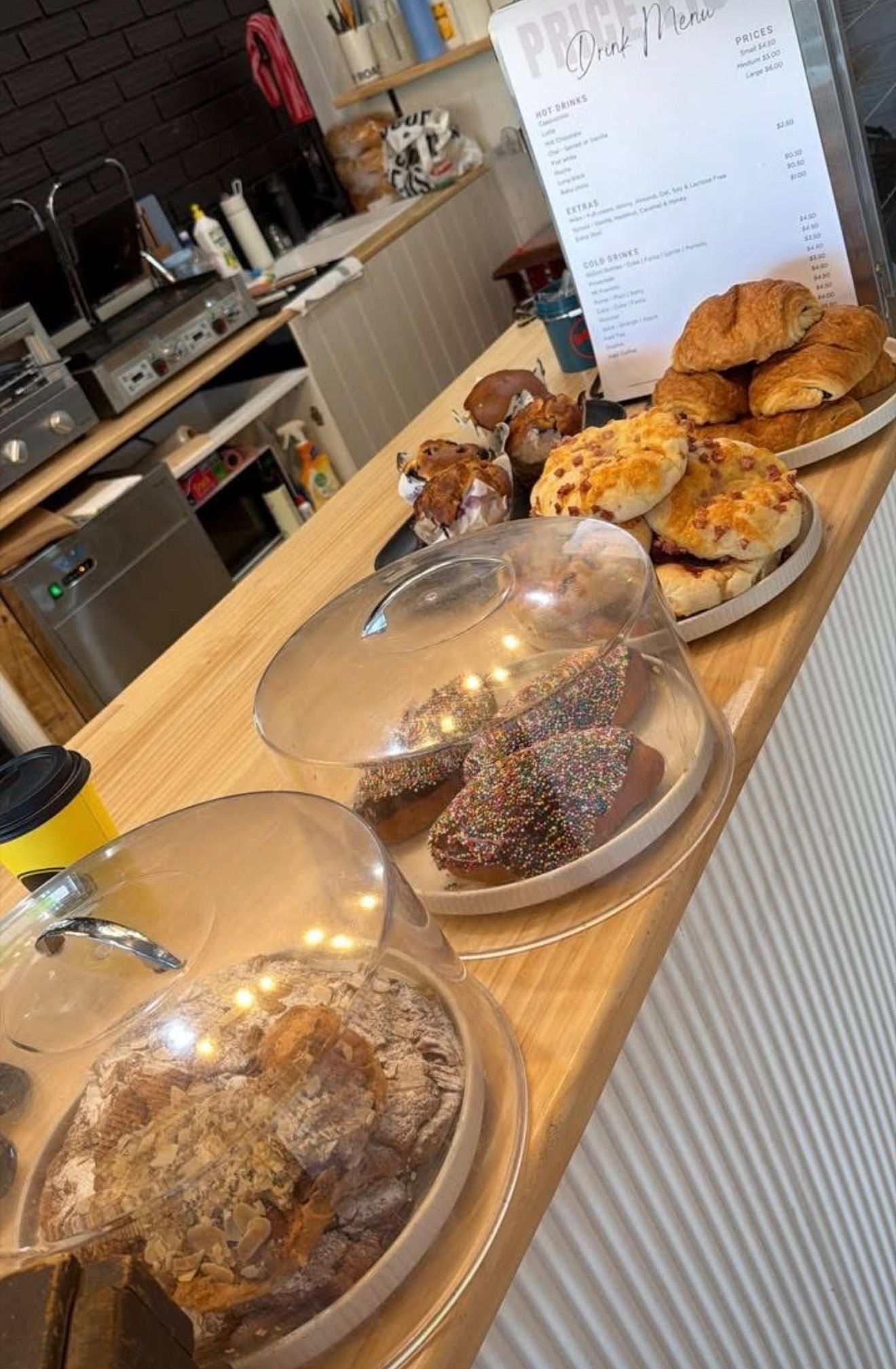 Counter view with cloche-covered buns, plates of pastries and a drink menu card