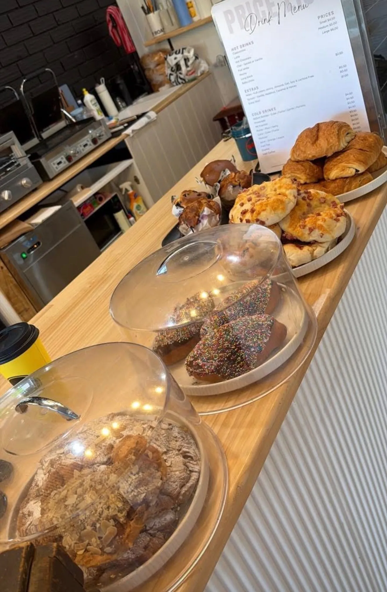 Counter view with cloche-covered buns, plates of pastries and a drink menu card